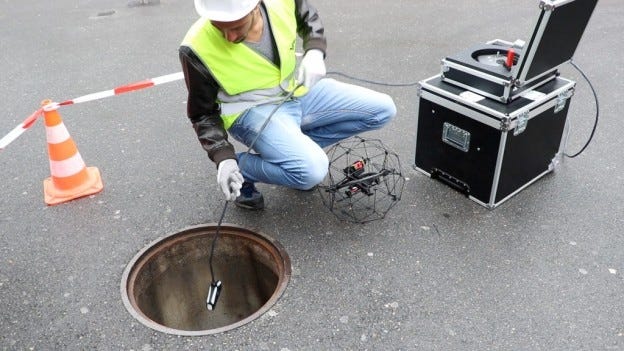 Technician using the Flyability Elios drone with a range extender for confined-space inspection inside a manhole, supporting industrial inspections, infrastructure maintenance, utility assessments, and hazardous environment operations.